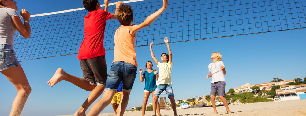 Big group of teenage boys and girls playing volleyball on the beach